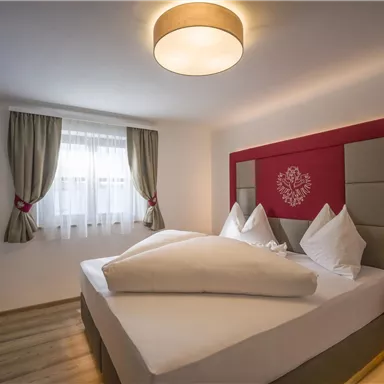 A modern bedroom with a large double bed and cozy furnishings. The windows are fitted with curtains and there is soft lighting.