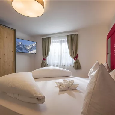 A cozy bedroom with a large bed and decorative pillows. The room features a television and a wooden wardrobe.