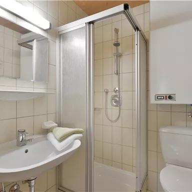 A modern bathroom view with a shower, sink, and toilet. The walls are brightly tiled and well-lit.