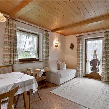 A cozy living space with a dining table, a sofa, and a window leading outside. The wood paneling creates a warm atmosphere.