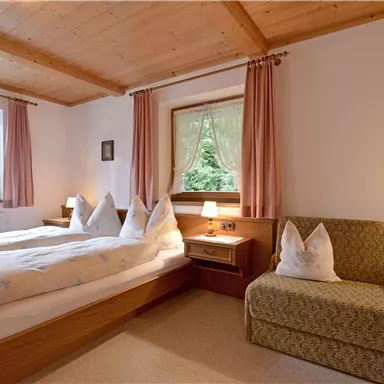A cozy bedroom with two beds and a small seating area. Large windows let in plenty of daylight and offer a view of the greenery.