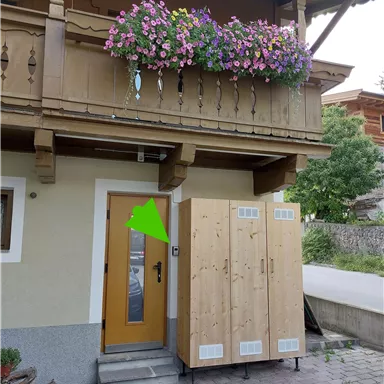 A cozy wooden house with a blooming balcony. In front of the door stands a large, wooden cupboard.