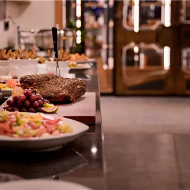 Ein raffiniertes Buffet mit verschiedenen Speisen, darunter Fleisch, Fleischgerichte und frisches Gemüse. Der Tisch ist elegant gedeckt und bietet eine einladende Atmosphäre.