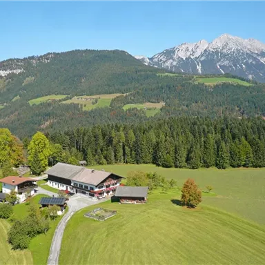 Eine malerische Landschaft mit einem Bauernhaus, umgeben von saftigem Grün und hohen Bergen im Hintergrund. Die klare Luft und die ruhige Umgebung schaffen eine idyllische Atmosphäre.