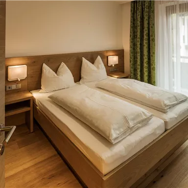 A modern bedroom with a double bed and two large pillows. The cozy atmosphere is accentuated by the wooden interior and the soft light sources.
