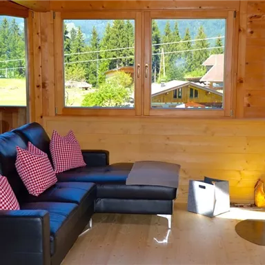 A cozy seating area with a black sofa and checked cushions. Large windows offer a view of the green landscape.