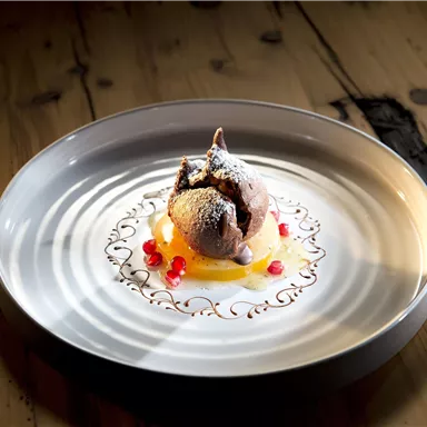 An artfully arranged dessert on a white plate. It consists of chocolate ice cream, orange fruit puree, and red berries.