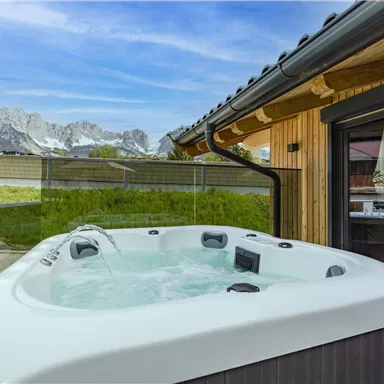 A whirlpool stands at a modern house overlooking the mountains. The surroundings are green and the atmosphere is calm and relaxing.