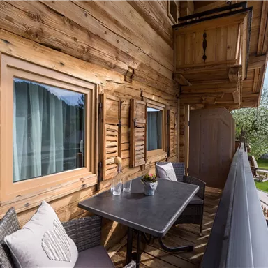 A cozy balcony with wood paneling and a table with chairs. In the background, a green garden can be seen.