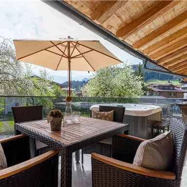 A cozy balcony with a table and chairs. In the background, there are trees and mountains.