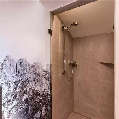 A modern shower with tiles in neutral colors. In the background, a mountain motif can be seen on the wall.