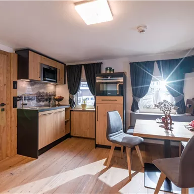 A modern kitchen with wooden cabinets and a small dining table. The light falls through a window, giving the room a friendly atmosphere.