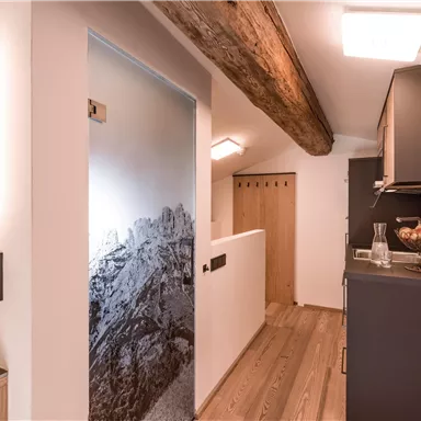 A modern hallway with wooden flooring and an elegant kitchen. The walls are light-colored and there is an interesting graphic-style door featuring mountain motifs.