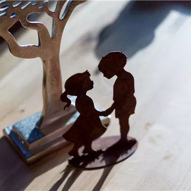 A delicate metal figure depicting a nanny and a boy holding hands. In the background, there is an ornate tree stand.