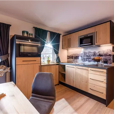 A modern kitchen with wooden cabinets and an elegant countertop. The room is bright and well-furnished with a table and chairs.