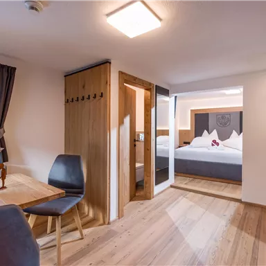 A modern room with wooden flooring and cozy furnishings. There is a dining area, a wardrobe, and an adjoining bedroom.