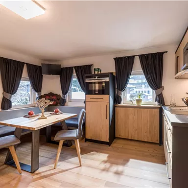 A cozy kitchen with a dining table and modern furniture. Large windows let in plenty of light and the room feels inviting.
