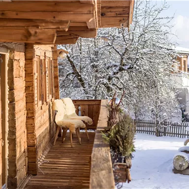 A wooden house with a decorated porch, surrounded by snow-covered trees. The quiet winter landscape conveys a cozy atmosphere.