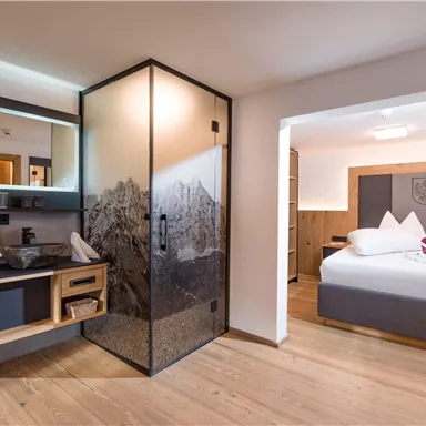 A modern hotel room with an elegant bathroom and a cozy sleeping area. The decor is stylish and bright, with wooden details and clean lines.