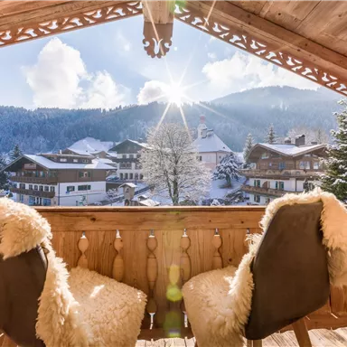 A cozy porch with two chairs and a view of snow-covered mountains. The sun shines brightly in the winter landscape.