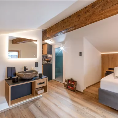 A modern bedroom with a large bed and wooden ceilings. A stylish wash area with a large mirror and a cozy atmosphere.
