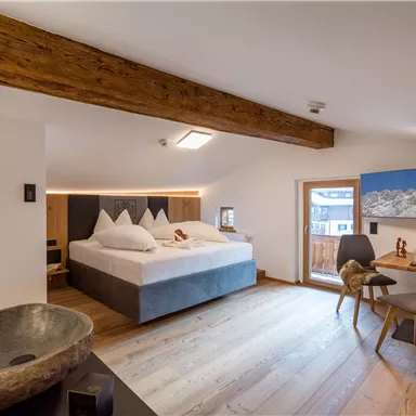 A modern room with a large bed, wooden ceiling, and neutral colors. There is a cozy workspace next to a window with a view of the mountains.