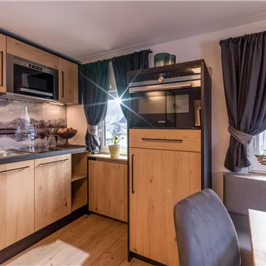A modern kitchen with wooden cabinets and built-in appliances. Large windows provide bright light and a cozy atmosphere.