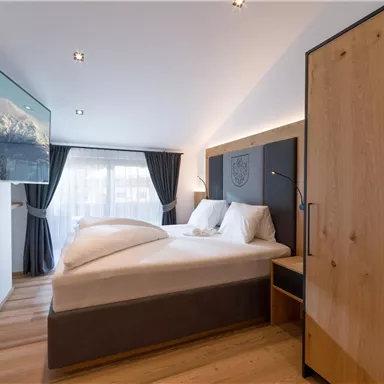 A modern bedroom with a large bed and a television on the wall. Bright colors and wooden details create a cozy atmosphere.