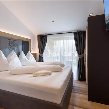 A modern hotel room with a large double bed and elegant pillows.  
Large windows provide plenty of daylight and an exterior view.