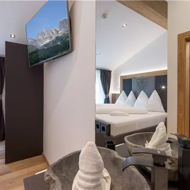 A modern bedroom with a large bed and a TV on the wall. The decor is minimalist with wooden elements and elegant details.