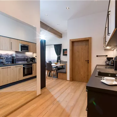 A modern kitchen with wooden cabinets and elegant appliances. In the background, there is a cozy dining area with a table and chairs.
