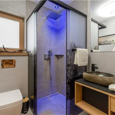 A modern bathroom with a shower and atmospheric blue lighting. The decor is simple and elegant, with natural materials.