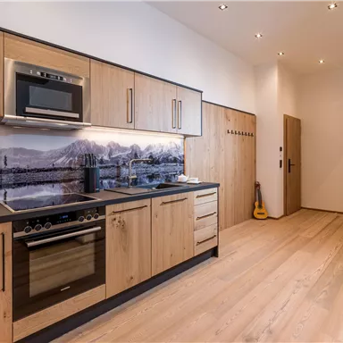 A modern kitchen with wooden cabinets and an elegant countertop. The room is bright and inviting, with a large window area and warm light.