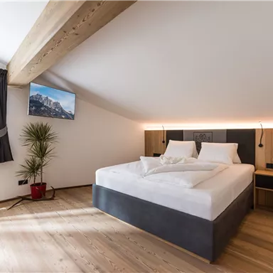 A modern bedroom with a large bed and a television on the wall. The wood details and the pleasant light create a cozy atmosphere.