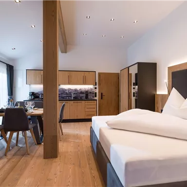 A modern room with a large double bed and wooden furniture. The dining area is well furnished and accommodates several people.