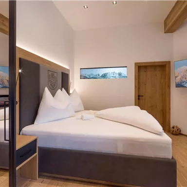 A modern bedroom with a large double bed and elegant wooden elements. The walls feature pictures of the mountains, and the room feels warm and inviting.