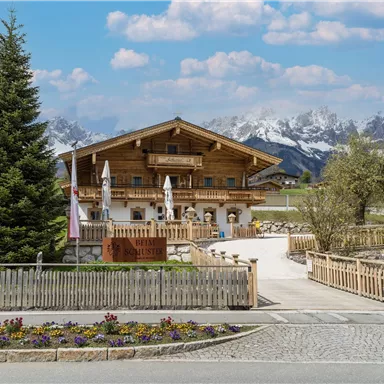 A charming wooden house with a blooming garden and a beautiful view of the mountains. The surroundings are green and inviting.