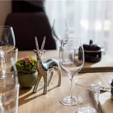 A beautifully set table with elegant glasses and a decorative silver antler. In the center stands a small plant in a pot.