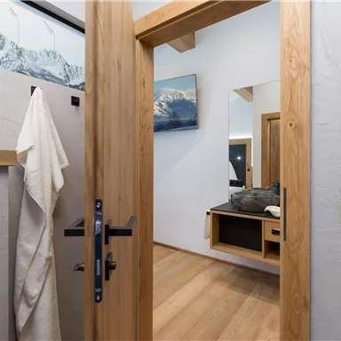 An inviting room with wooden details and bright light. In the background, there is a mirror and a modern dresser.