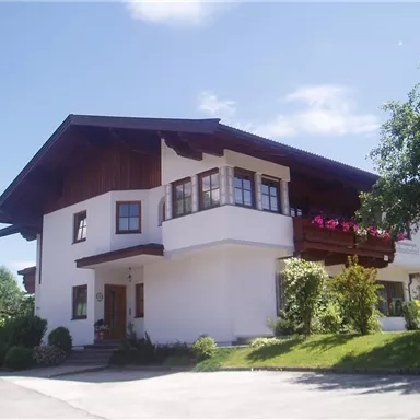 An appealing two-story house with a beautiful balcony and plants. The surroundings are green and sunny, ideal for a cozy home.