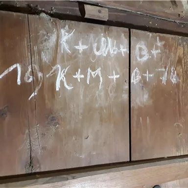 Eine Holzoberfläche mit handgeschriebenen Zeichen und Formeln in weißer Farbe. Die Inhalte scheinen mathematische Notationen oder Notizen zu sein.
