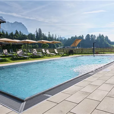 A refreshing pool with clear water and a towel beside it. On the edge, there is a carafe with a drink and glasses.