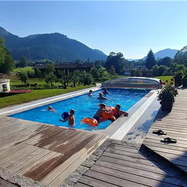 Ein schöner Pool in einer sonnigen Landschaft. Menschen genießen das Wasser und die Aussicht auf die Berge.