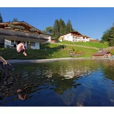 A peaceful pond surrounded by trees and beautiful scenery. In the background, several buildings can be seen, ideal for a relaxing stay.