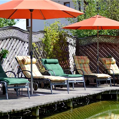 A cozy terrace with lounge chairs and sun umbrellas. In the background, plants and a fence can be seen.
