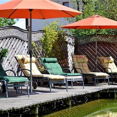 A relaxing terrace with deck chairs and sun umbrellas. In the background, a tranquil pond can be seen.