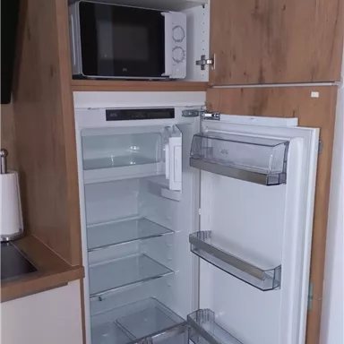 A modern refrigerator with transparent compartments and a clean, tidy interior view. At the top, there is a microwave and some kitchen appliances.