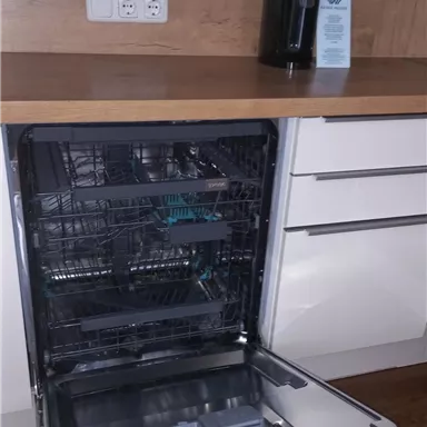 A modern kitchen with an open dishwasher and a wooden countertop. On the counter, there is a water dispenser.