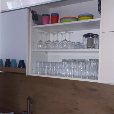 A modern kitchen with an open kitchen shelf. Glasses, mugs, and a carafe are on a wooden shelf.