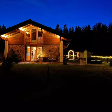 Das Almchalet Weberhof mit warmem Licht im Dunkeln. Der Garten ist gemütlich und von Bäumen umgeben.